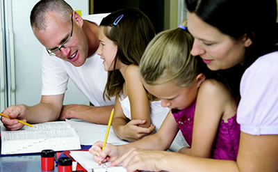 mother and father sitting at a desk with their 2 daughters, tutoring them with their school work